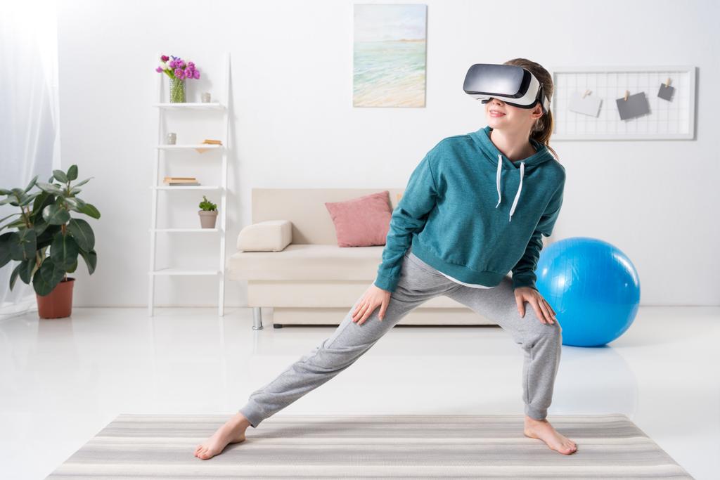 meisje uitrekken benen met virtual reality headset op yoga mat thuis - Foto, afbeelding