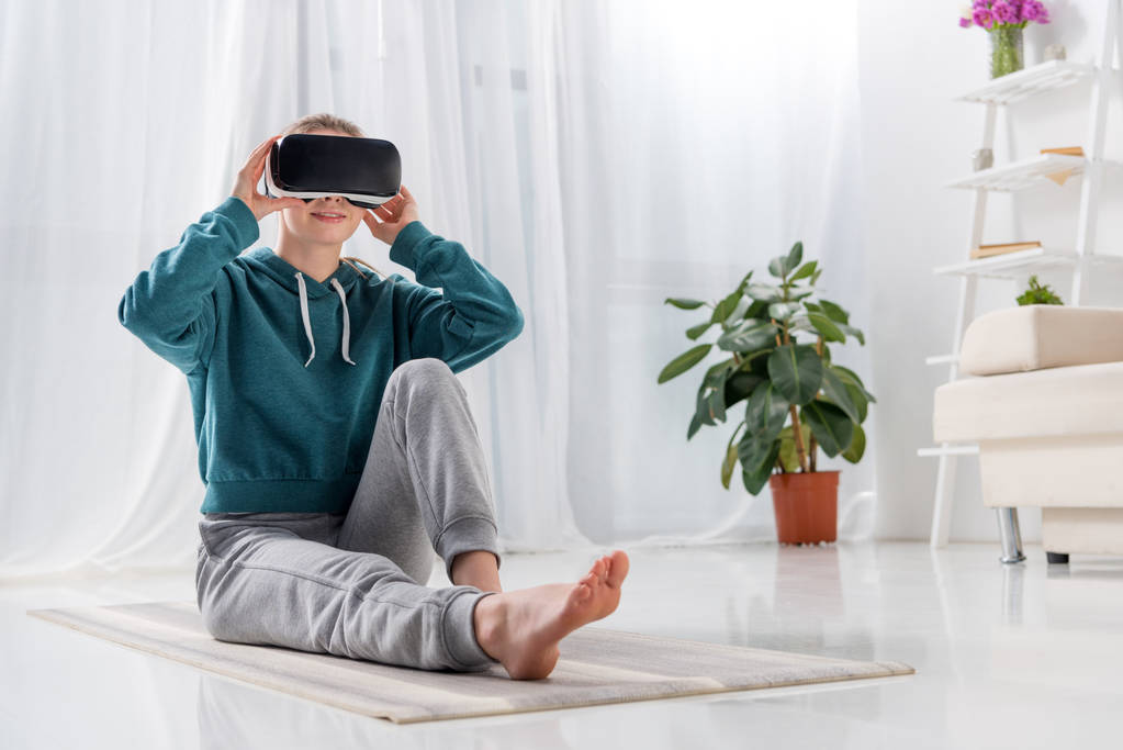 dziewczyna siedzi na matę do jogi z zestaw wirtualnej rzeczywistości w domu - Zdjęcie, obraz