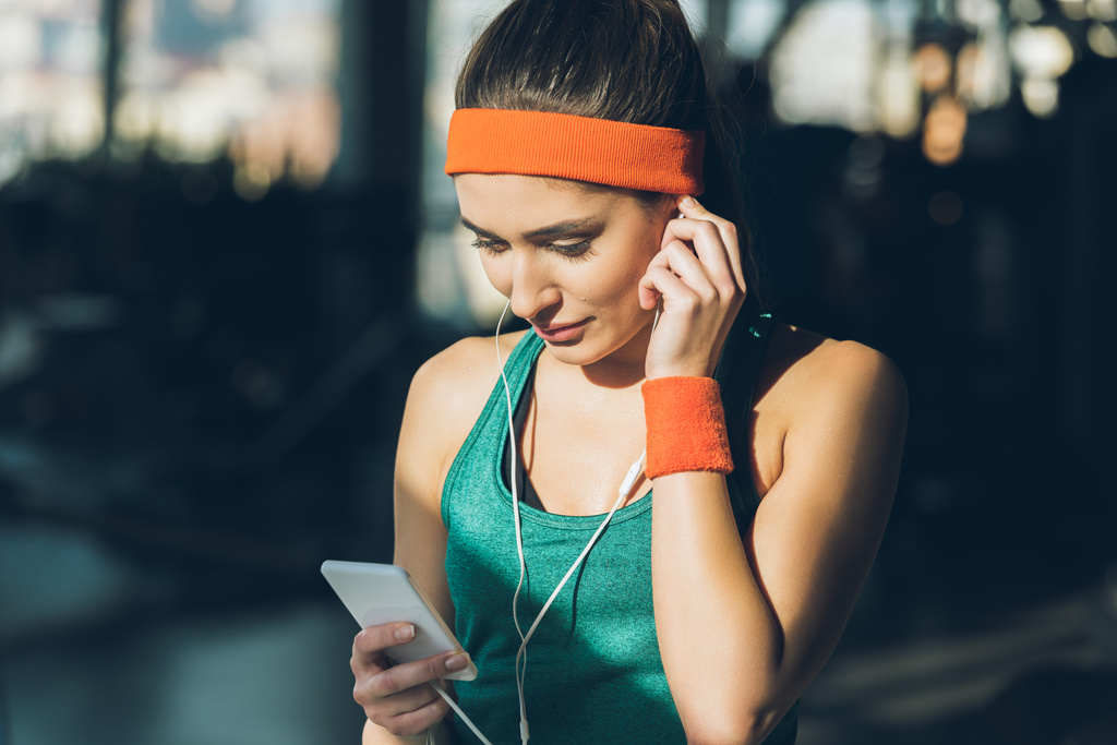 sportovní žena pomocí chytrého telefonu a sluchátka v tělocvičně - Fotografie, Obrázek