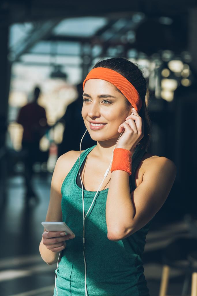 uśmiechnięta kobieta za pomocą smartfona i słuchawki w siłowni  - Zdjęcie, obraz