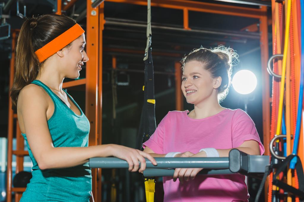 sporty woman standing against beams and smiling to overweight woman  - Photo, Image