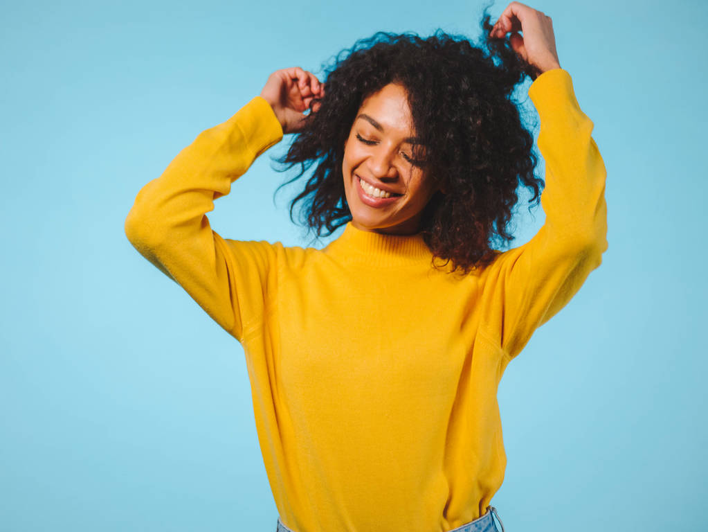 Primer plano retrato de la mujer afroamericana riendo aislada sobre fondo azul. Mezcla de raza chica en amarillo desgaste posando en estudio
. - Foto, imagen