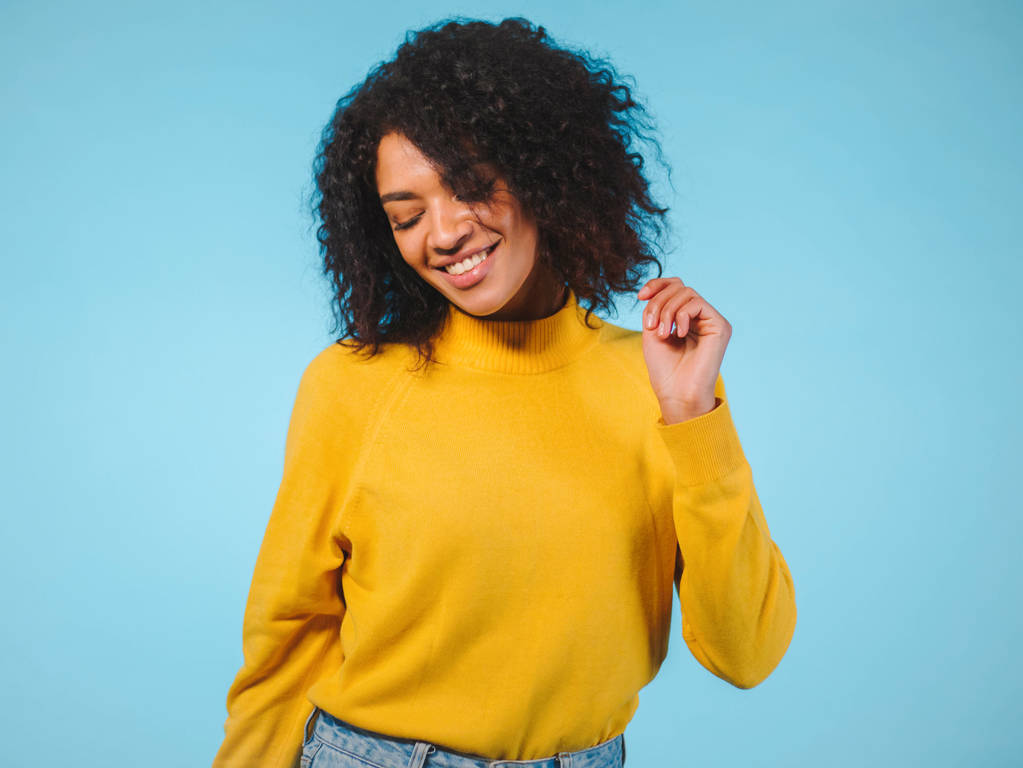 Primer plano retrato de la mujer afroamericana riendo aislada sobre fondo azul. Mezcla de raza chica en amarillo desgaste posando en estudio
. - Foto, Imagen