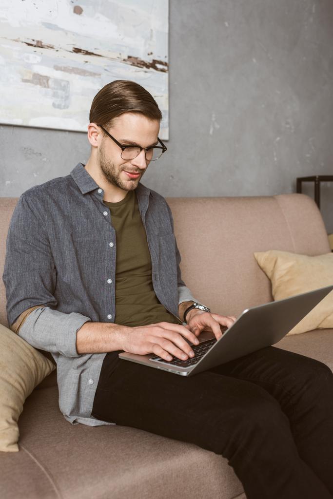 happy stylish man working with laptop on couch - Photo, Image