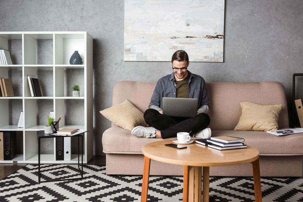 jovem freelancer feliz trabalhando com laptop enquanto sentado no sofá
 - Foto, Imagem