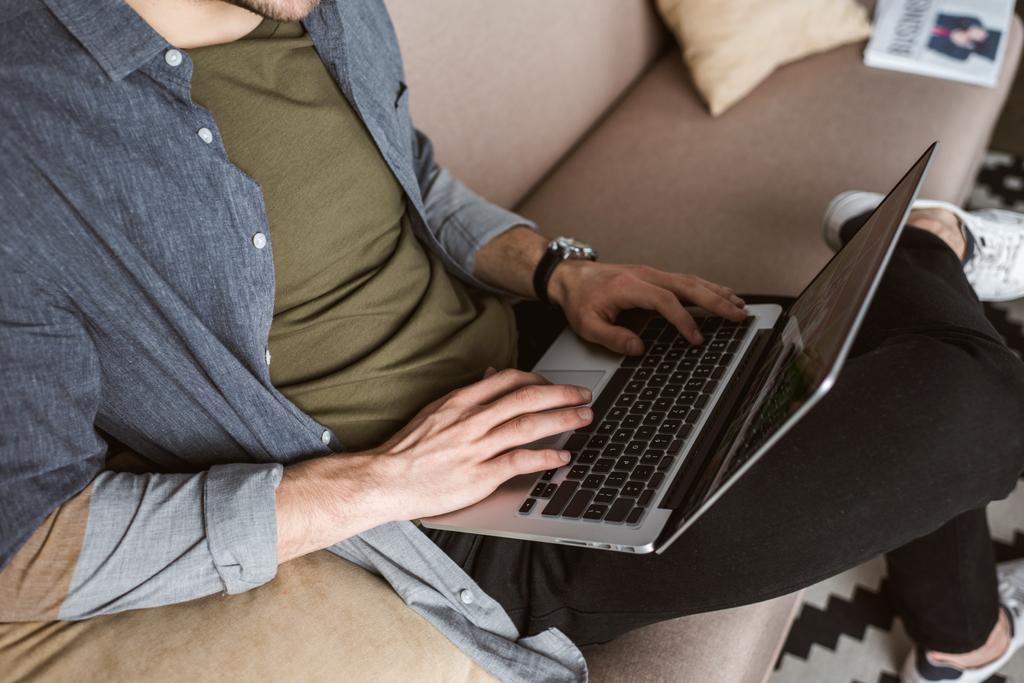 обрезанный снимок человека, работающего с ноутбуком на диване
 - Фото, изображение