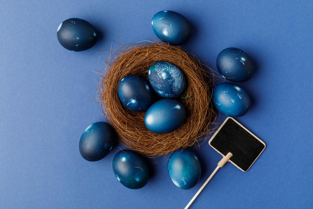 κάτοψη του μπλε βαμμένα αυγά του Πάσχα σε διακοσμητικά φωλιά σε μπλε επιφάνεια - Φωτογραφία, εικόνα