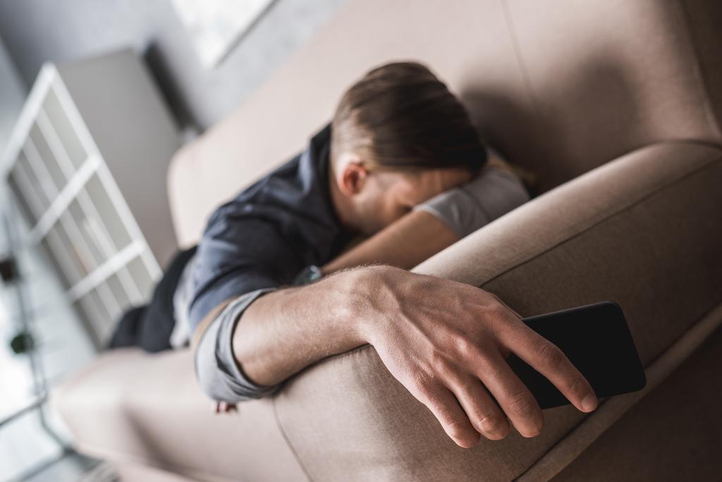 tired young man sleeping on couch with smartphone in hand - Photo, Image