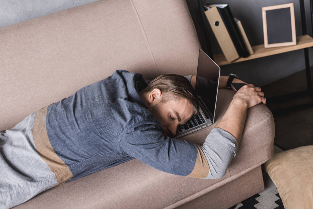 jeune homme d'affaires surmené dormant sur le canapé avec la tête couchée sur un ordinateur portable
 - Photo, image