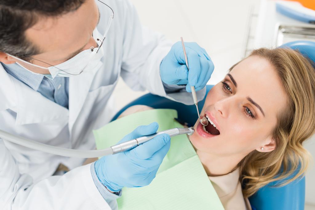 Пациентка на стоматологической процедуре с использованием зубной дрели в современной стоматологической клинике
 - Фото, изображение
