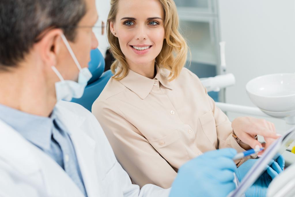 Vrouw in overleg met de tandarts kijken naar Klembord in moderne kliniek - Foto, afbeelding