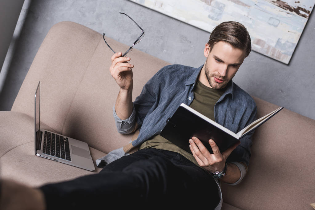 молодий серйозний бізнесмен читає нотатки на дивані
 - Фото, зображення