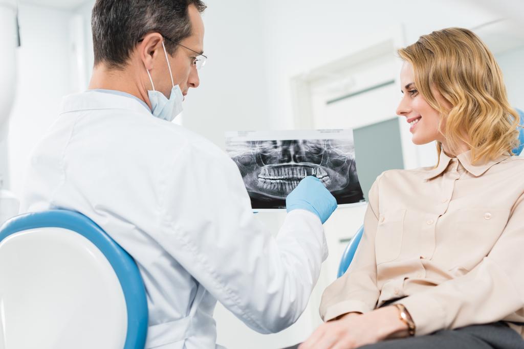 Vrouw in overleg met de tandarts kijken x-ray in moderne kliniek - Foto, afbeelding