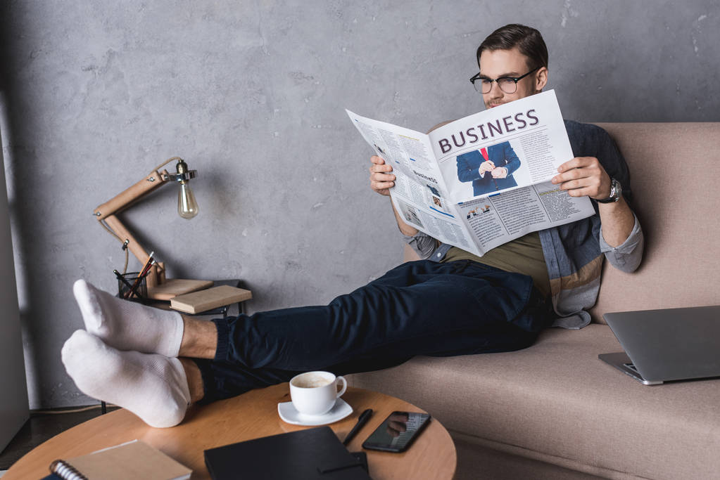 young barefoot businessman reading newspaper on couch - Photo, Image