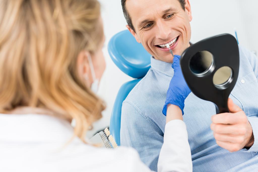 Ο άνθρωπος που επιλέγουν δοντιών εμφυτεύματος κοιτάζοντας καθρέφτη σε σύγχρονο οδοντιατρείο - Φωτογραφία, εικόνα