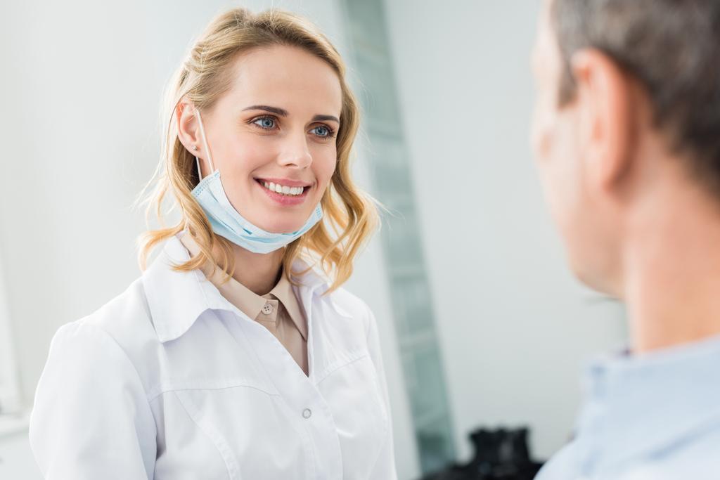 Χαμογελαστός ο γιατρός ακούει ασθενή σε σύγχρονο οδοντιατρείο - Φωτογραφία, εικόνα