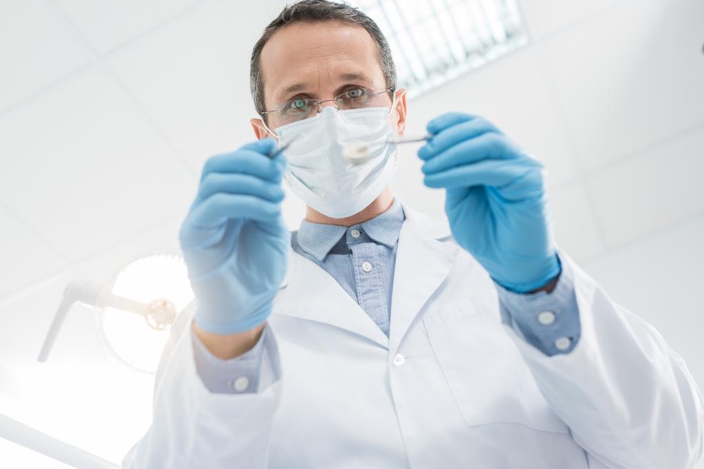 Дантист проверяет зубы пациента с зеркалом в современной клинике - Фото, изображение