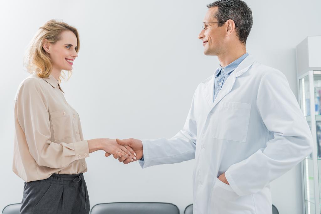 В современной стоматологической клинике мужчина и женщина пожимают руку пациентке
 - Фото, изображение