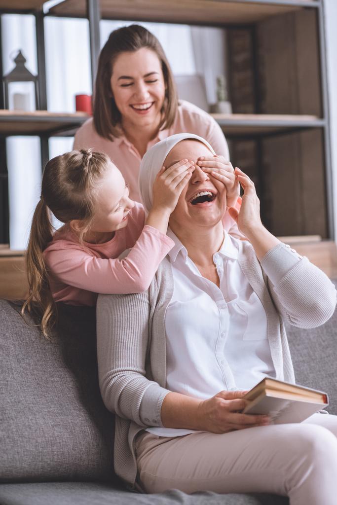 счастливая мать и дочь навещают больную улыбающуюся бабушку в книге чтения с платком дома
  - Фото, изображение