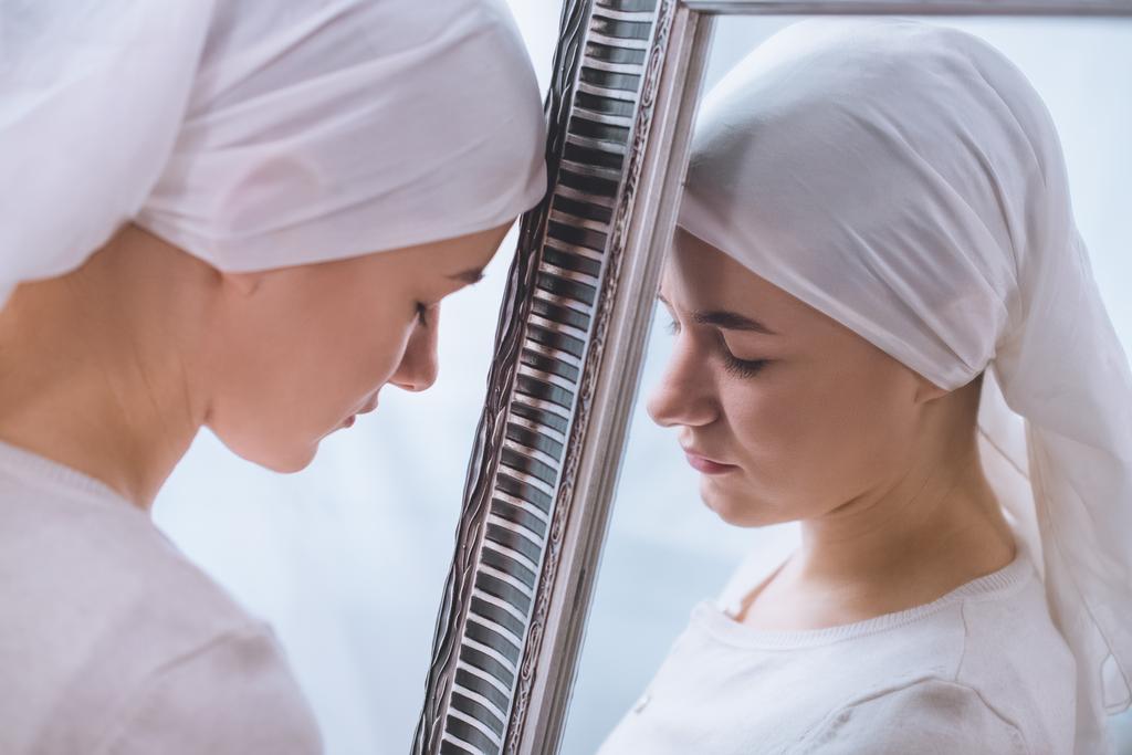 visão lateral da jovem mulher doente em kerchief inclinando-se ao espelho
 - Foto, Imagem