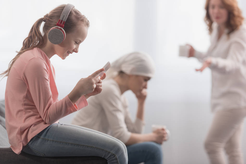 kid in headphones using digital tablet while sick mother and grandmother talking behind  - Photo, Image