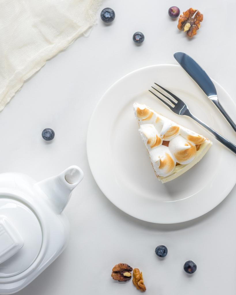 Draufsicht auf appetitanregendes Stück Kuchen mit Baiser und Teekanne auf weißem Tisch - Foto, Bild