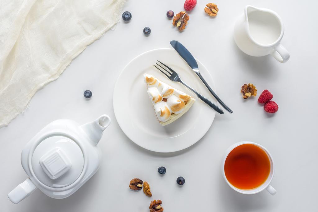 вид сверху на кусок торта с ягодами и чаем на белом столе
 - Фото, изображение
