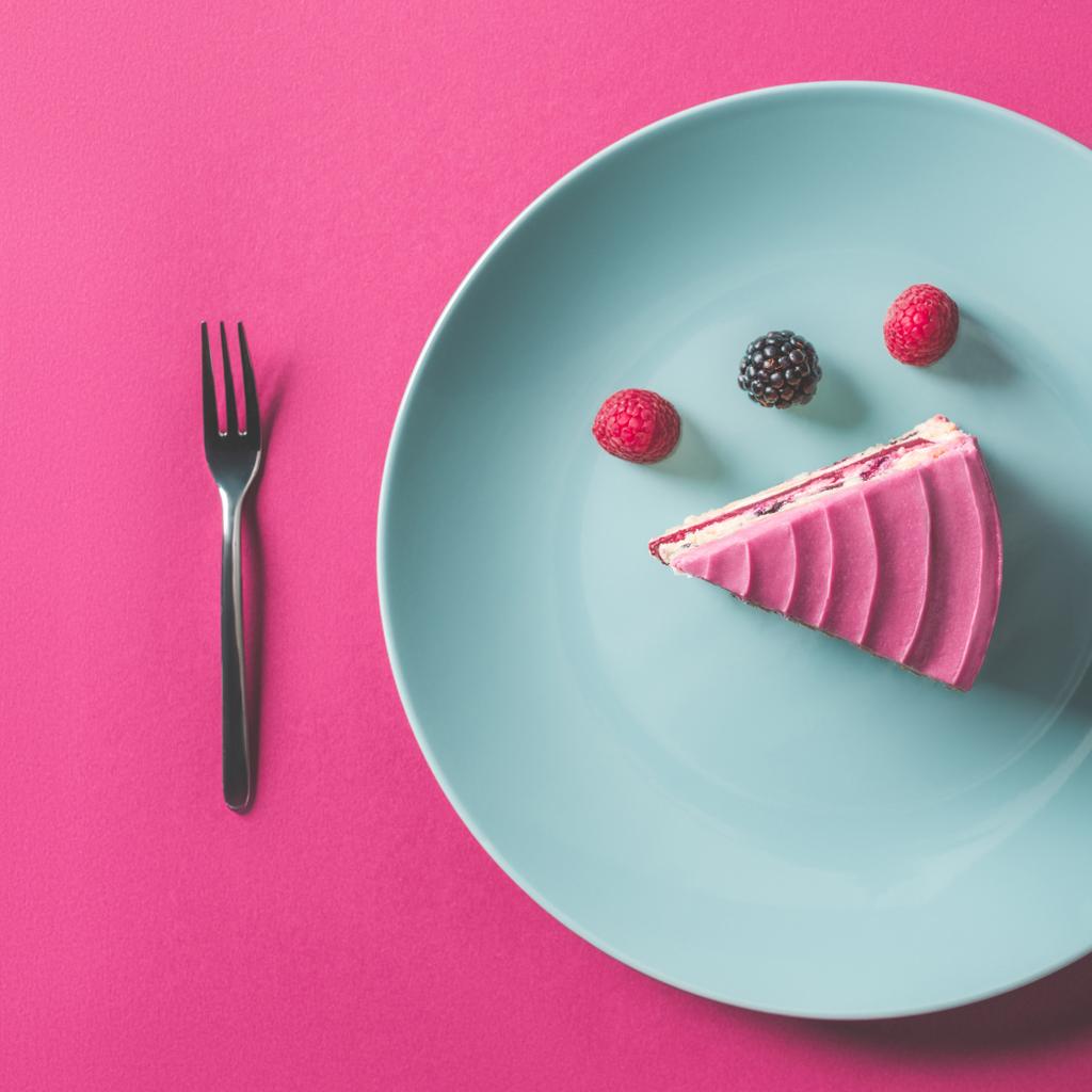 stuk van roze taart met bessen op plaat op roze oppervlak (bovenaanzicht) - Foto, afbeelding
