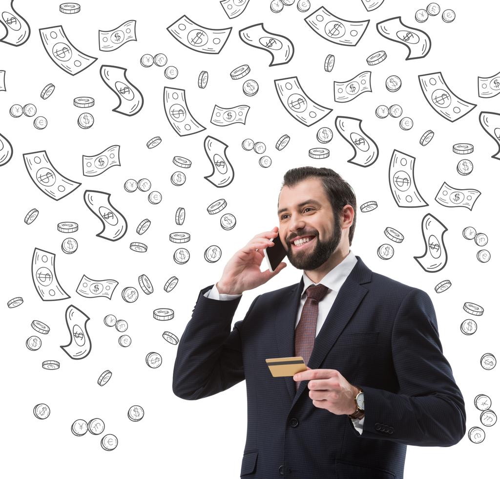 zakenman met credit card praten op smartphone, dollar biljetten en munten symbolen geïsoleerd op wit - Foto, afbeelding