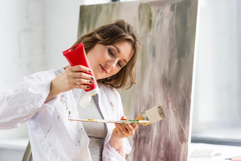 Jeune fille créative serrant tube de peinture dans le studio de lumière
 - Photo, image