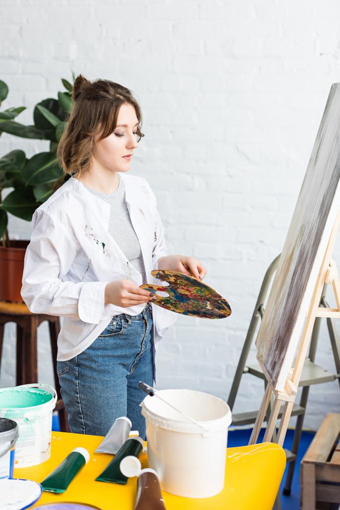 Молодая артистка с палитрой в светлой студии
 - Фото, изображение