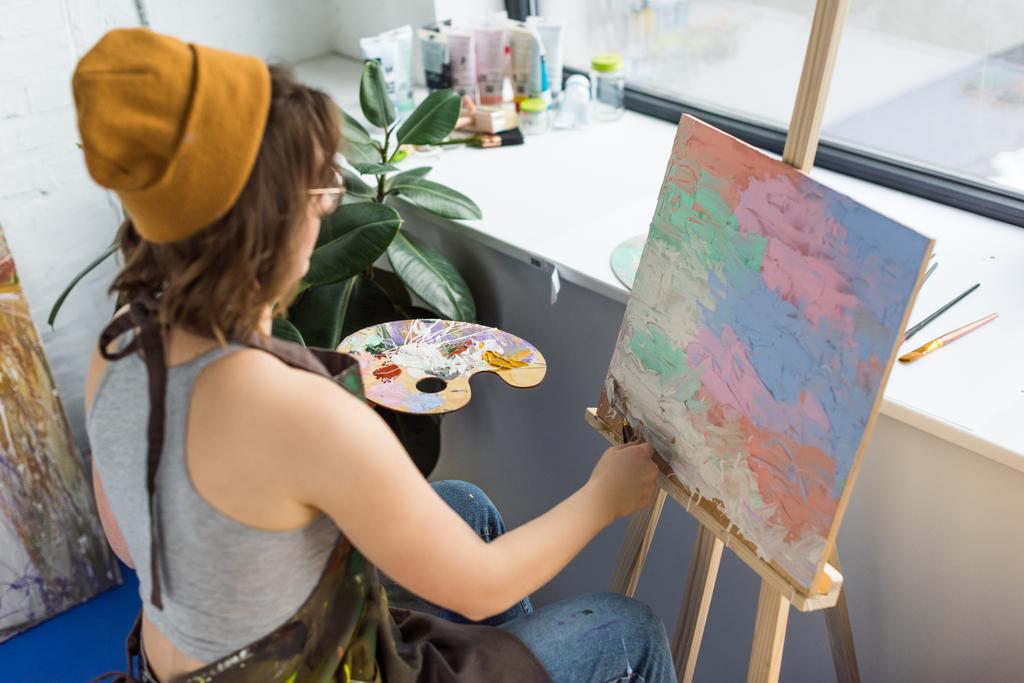 Молодая художница, работающая с ножом и холстом в светлой студии
 - Фото, изображение