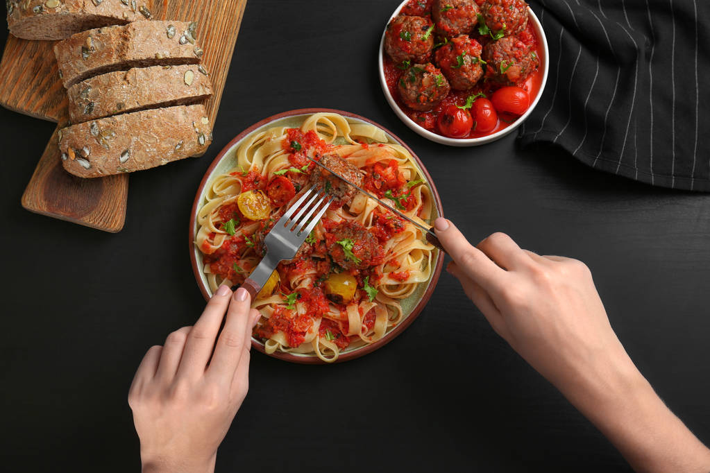 Mujer comiendo deliciosa pasta con bolas de carne y salsa de tomate en la mesa
 - Foto, imagen