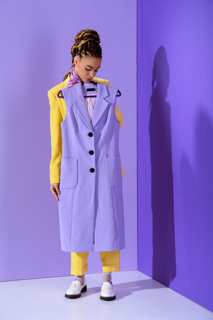 elegant african american girl in yellow suit holding purple waistcoat, on trendy ultra violet background - Photo, Image