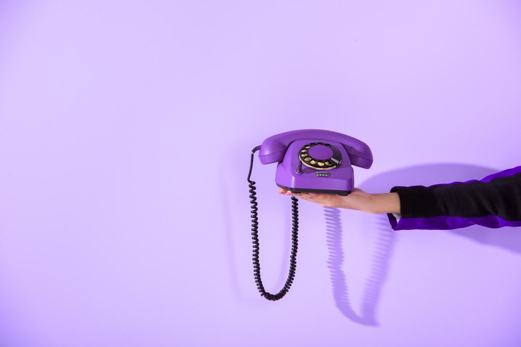 обрізаний вид дівчини, що тримає старовинний роторний телефон на ультрафіолетовій стіні
  - Фото, зображення