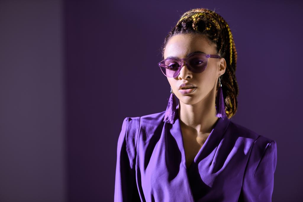 muodikas afrikkalainen amerikkalainen tyttö poseeraa trendikäs ultra violetti takki ja aurinkolasit
 - Valokuva, kuva