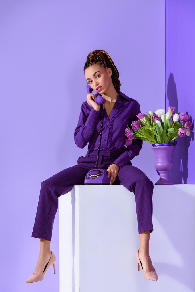 Elegantes Mulattin am Telefon und auf Würfel mit Tulpenstrauß sitzend - Foto, Bild