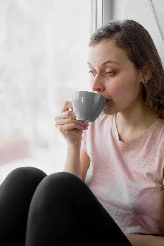 красива жінка п'є чай вранці, сидячи біля вікна
 - Фото, зображення