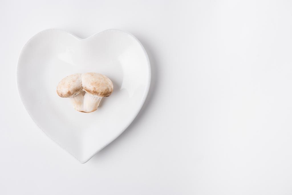 raw mushrooms laying on heart shaped plate on white background - Photo, Image