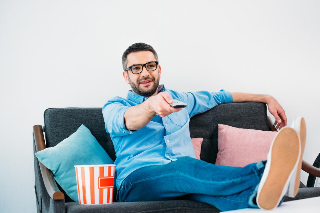 mies silmälaseissa lepää sohvalla ja katselee televisiota kotona
 - Valokuva, kuva