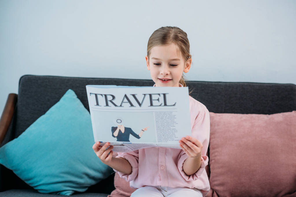 portrait of cute child reading travel newspaper while resting on sofa - Photo, Image