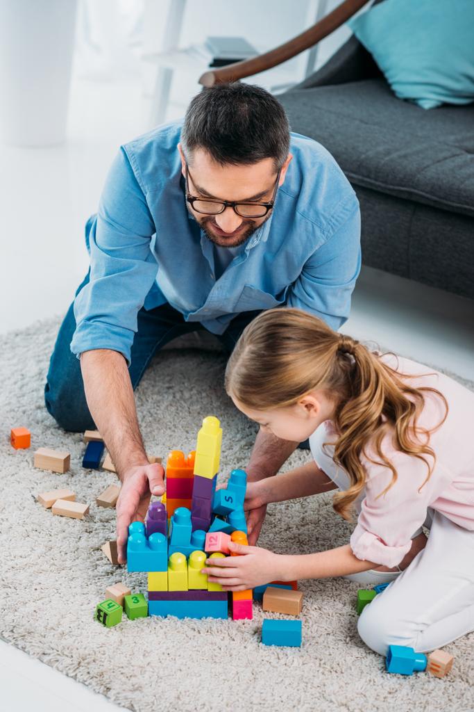 little daughter and father playing with colorful blocks together on floor at home - Photo, Image