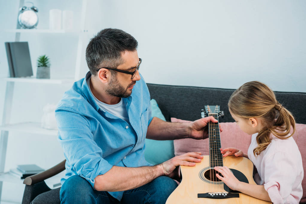 vue latérale du père enseignant fille jouer de la guitare à la maison
 - Photo, image