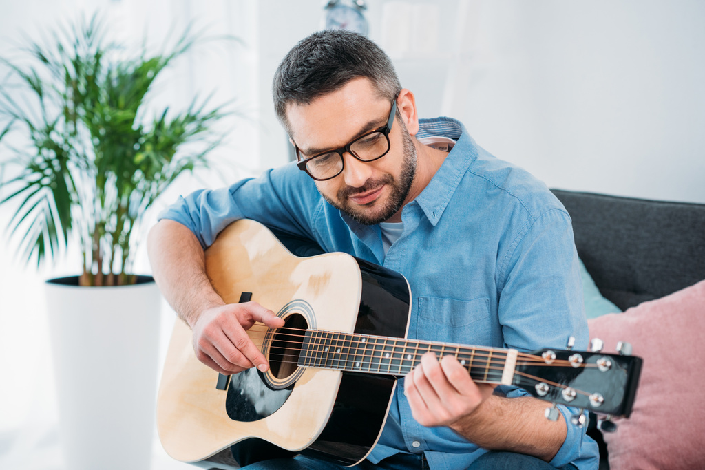 Portret van man in brillen spelen van akoestische gitaar thuis - Foto, afbeelding