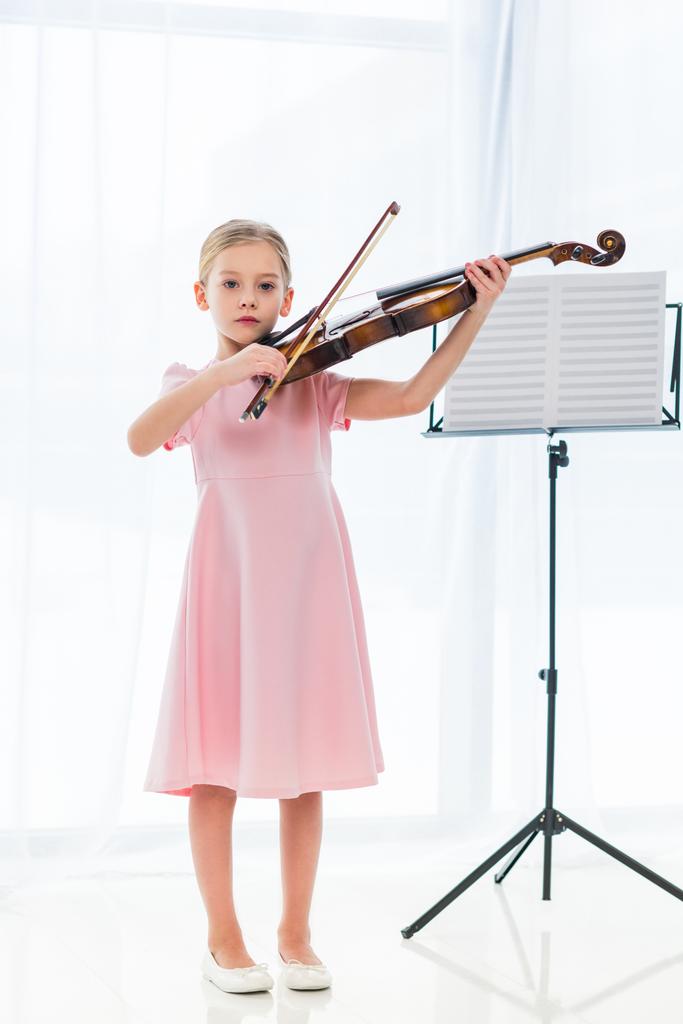 χαριτωμένο μικρό παιδί σε ροζ φόρεμα παίζει βιολί στο σπίτι - Φωτογραφία, εικόνα