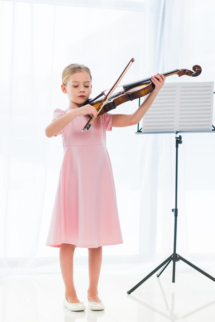 lindo niño en vestido rosa tocando el violín en casa
 - Foto, imagen