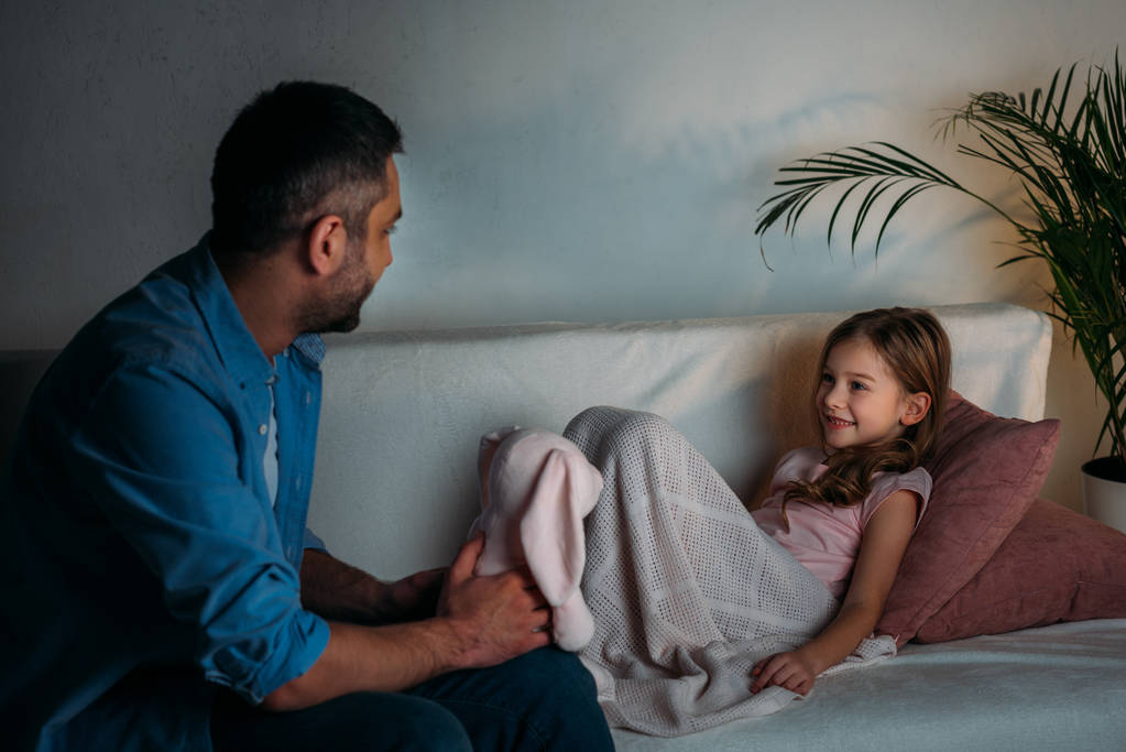 sivunäkymä hymyilevä tytär katselee isää lelu käsissä kotona
 - Valokuva, kuva