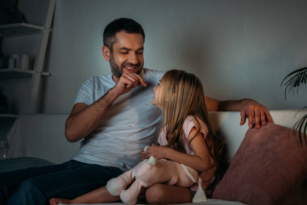 padre jugando con su hija pequeña mientras descansa en el sofá por la noche
  - Foto, Imagen