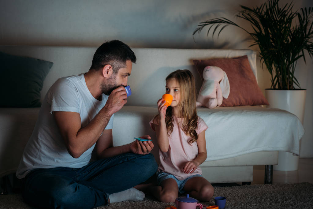 Vater und Tochter geben vor, zu Hause gemeinsam Tee zu trinken - Foto, Bild