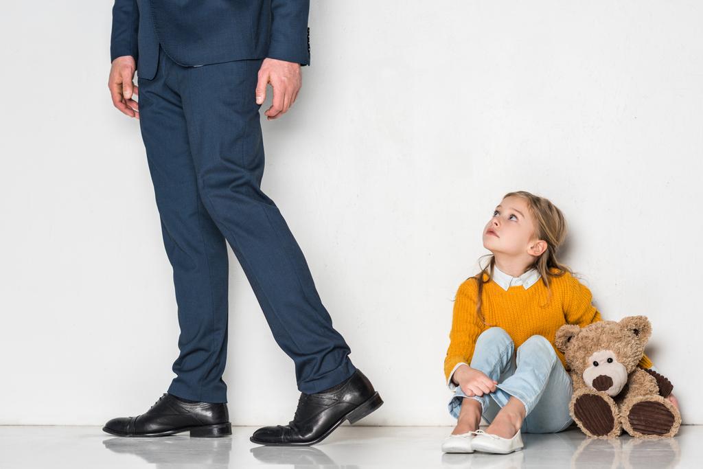 Aufgebrachte Tochter sieht Vater im Geschäftsanzug vereinzelt auf grauem Grund davonlaufen - Foto, Bild